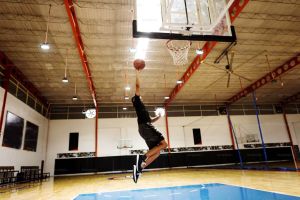 Quadra de basquete iluminada com high bey e uma pessoa fazendo cesta 